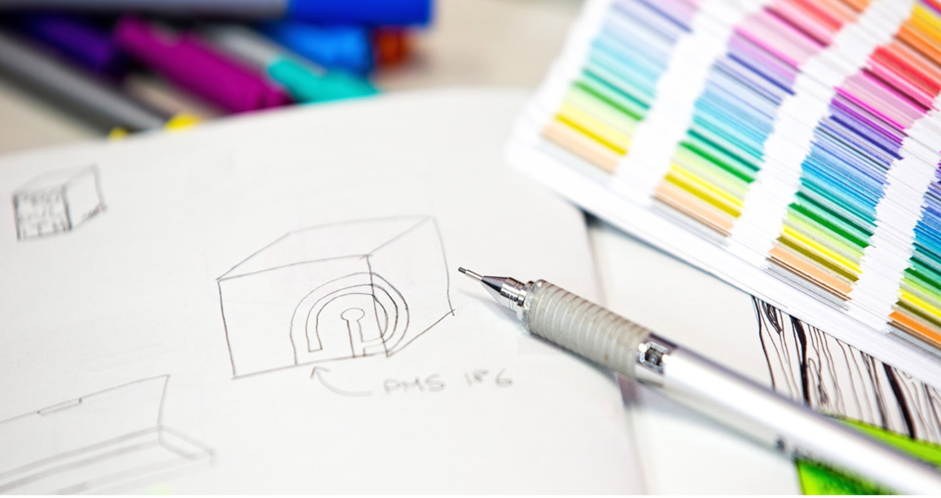 Photo montrant un croquis de conception d'emballage sur une feuille de papier, avec un stylo et une palette de couleurs à côté.