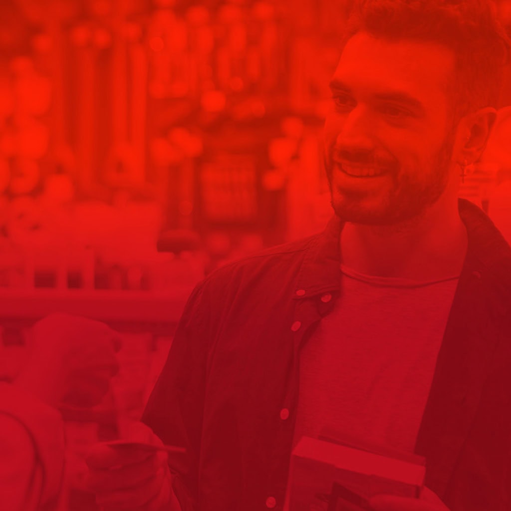 Homme souriant dans un magasin, tenant un produit dans ses mains, avec un filtre rouge sur l'image.