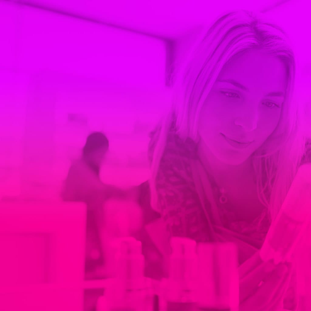 Femme blonde examinant un produit sur une étagère dans un magasin, avec un filtre rose sur l'image.